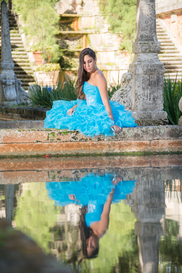Quinceañera on blue dress reflecting on water at Vizcaya Museum.